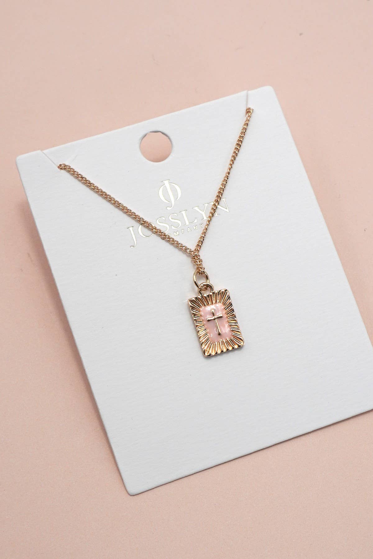 Gold Necklace with a pink cross pendant on a white card with 'Jewelry' branding, against a beige background