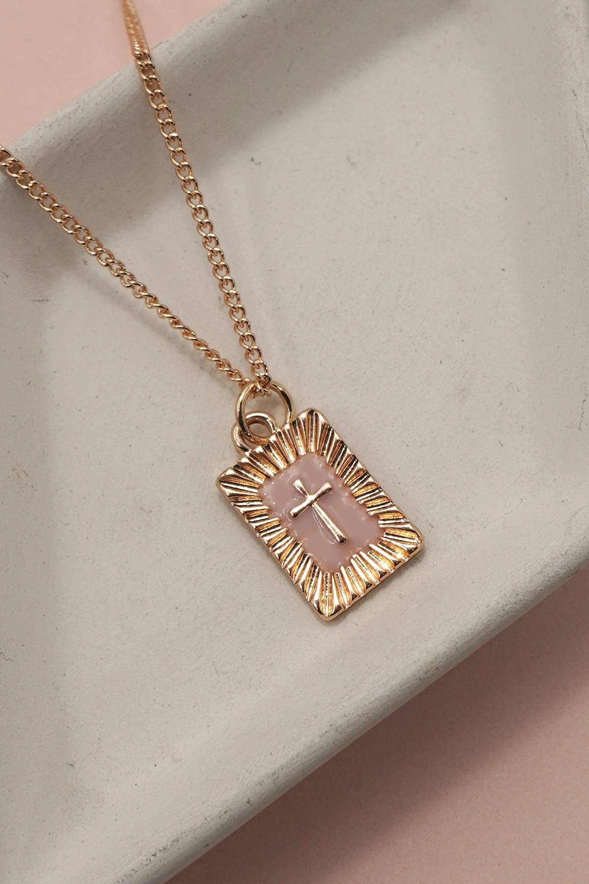 Gold necklace with a pink cross pendant on a light gray surface