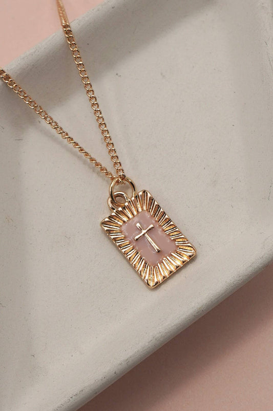 Gold necklace with a pink cross pendant on a light gray surface