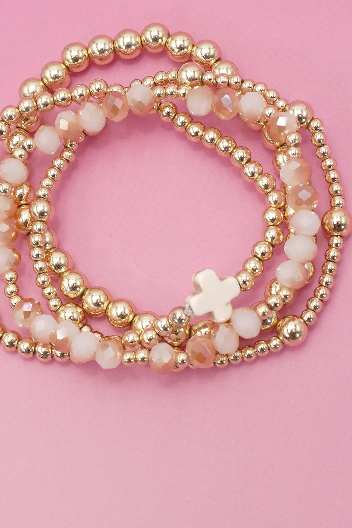 Stack of gold and white beaded bracelets on a pink background