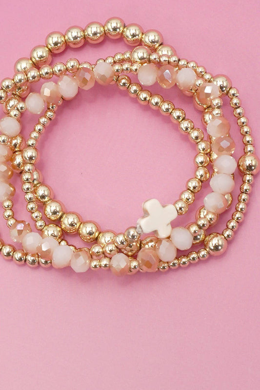 Stack of gold and white beaded bracelets on a pink background