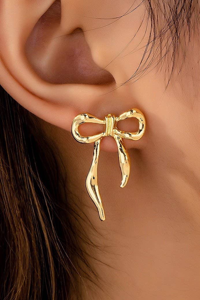 Gold bow-shaped earring worn on an ear with a blurred background