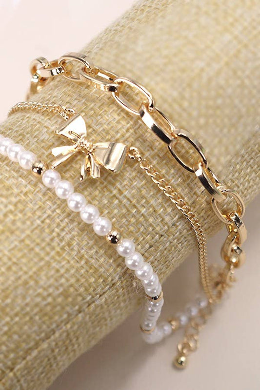 Gold chain bracelet with a bow charm and pearl bracelet on a beige fabric background