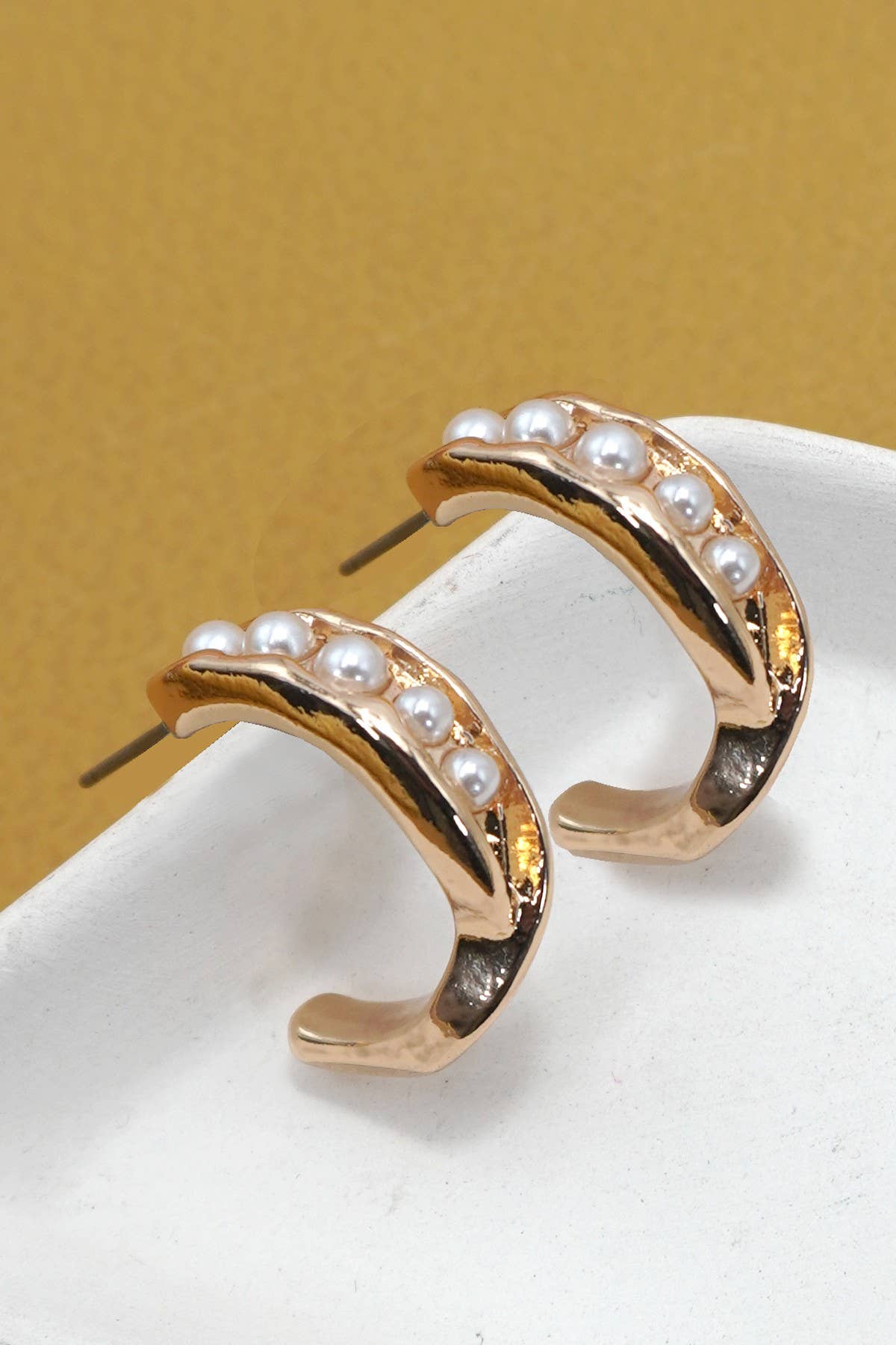 Gold hoop earrings with pearl accents on a white surface with a beige background