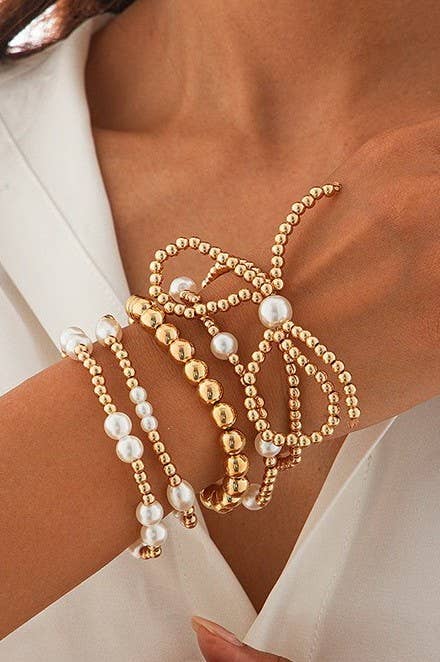 Gold and pearl beaded bracelets on a person's wrist against a neutral background