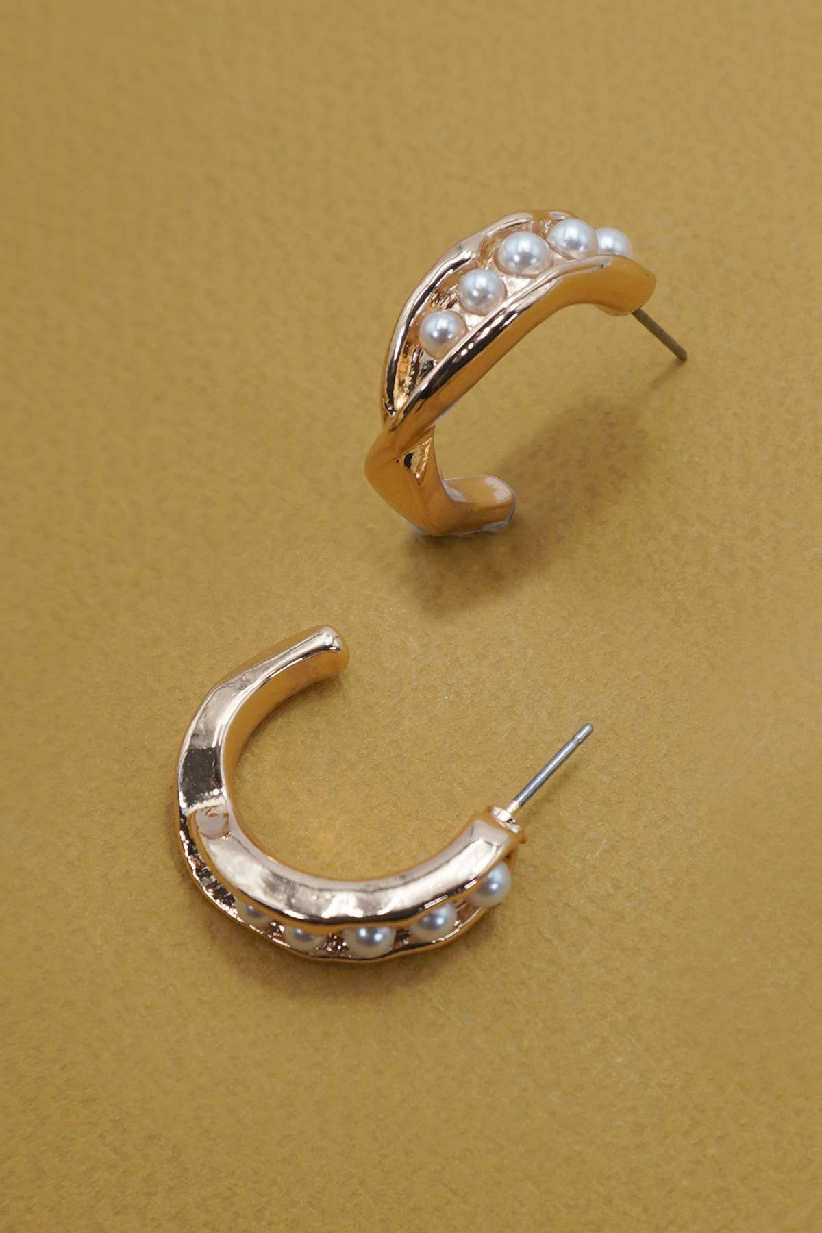 Gold hoop earrings with embedded pearls on a beige background