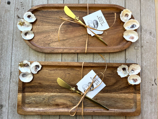 Two wooden trays with gold utensils and oysters on a wooden surface
