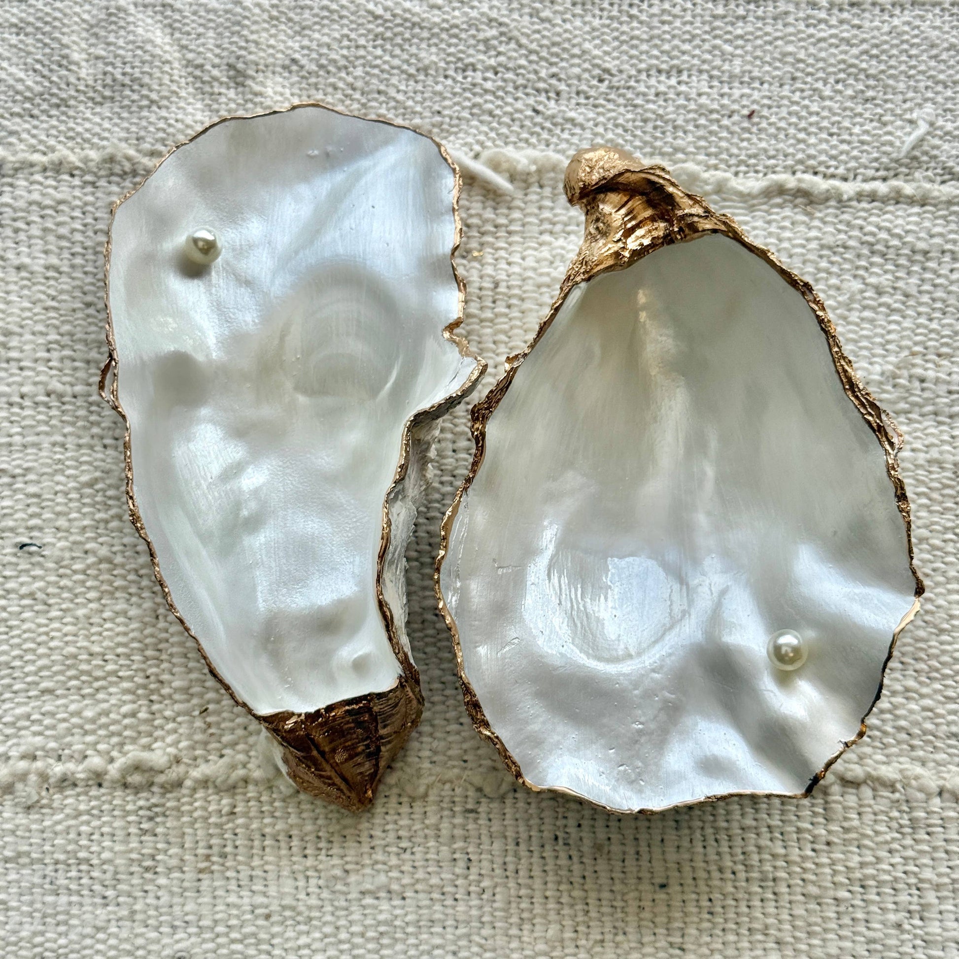 Two oyster shell jewelry dish with pearls on a textured fabric background