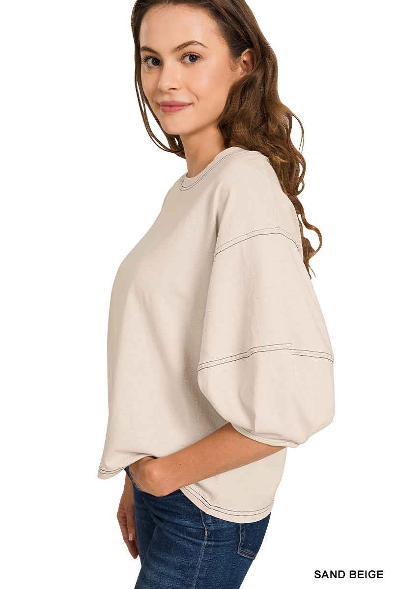 Woman wearing a sand beige top and blue jeans on a white background