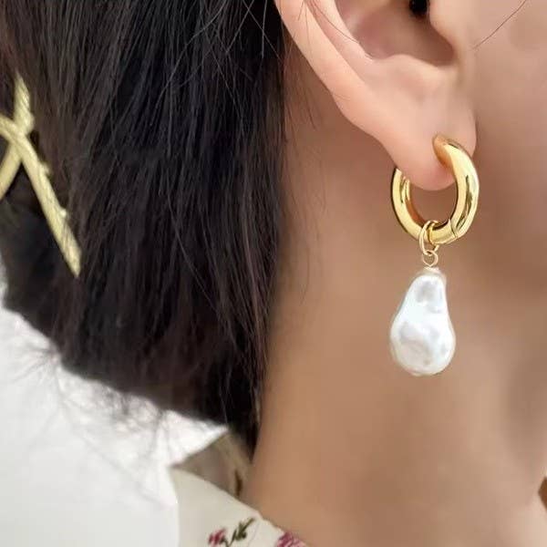 Gold hoop earring with a pearl charm worn by a person.