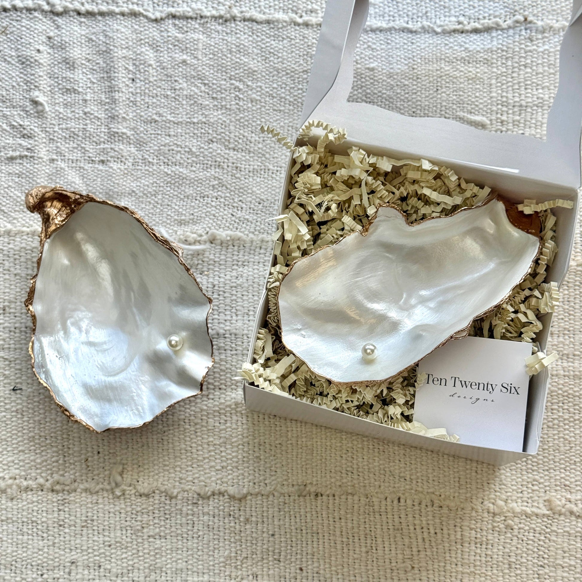 Pearl oyster jewelry dish with pearls inside a branded box on a textured fabric background