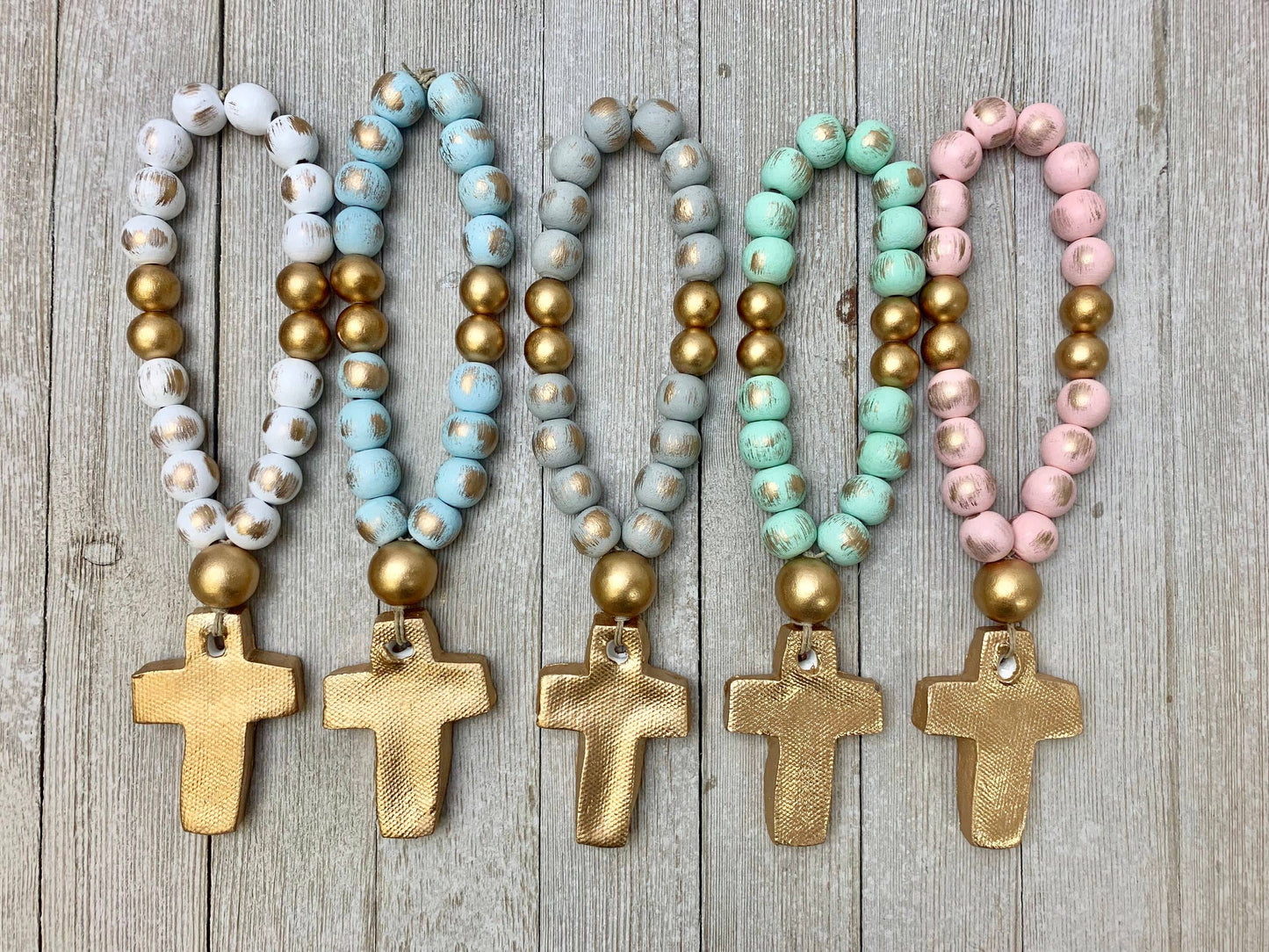Set of five beaded baby blessing beads with cross pendants on a wooden surface. 