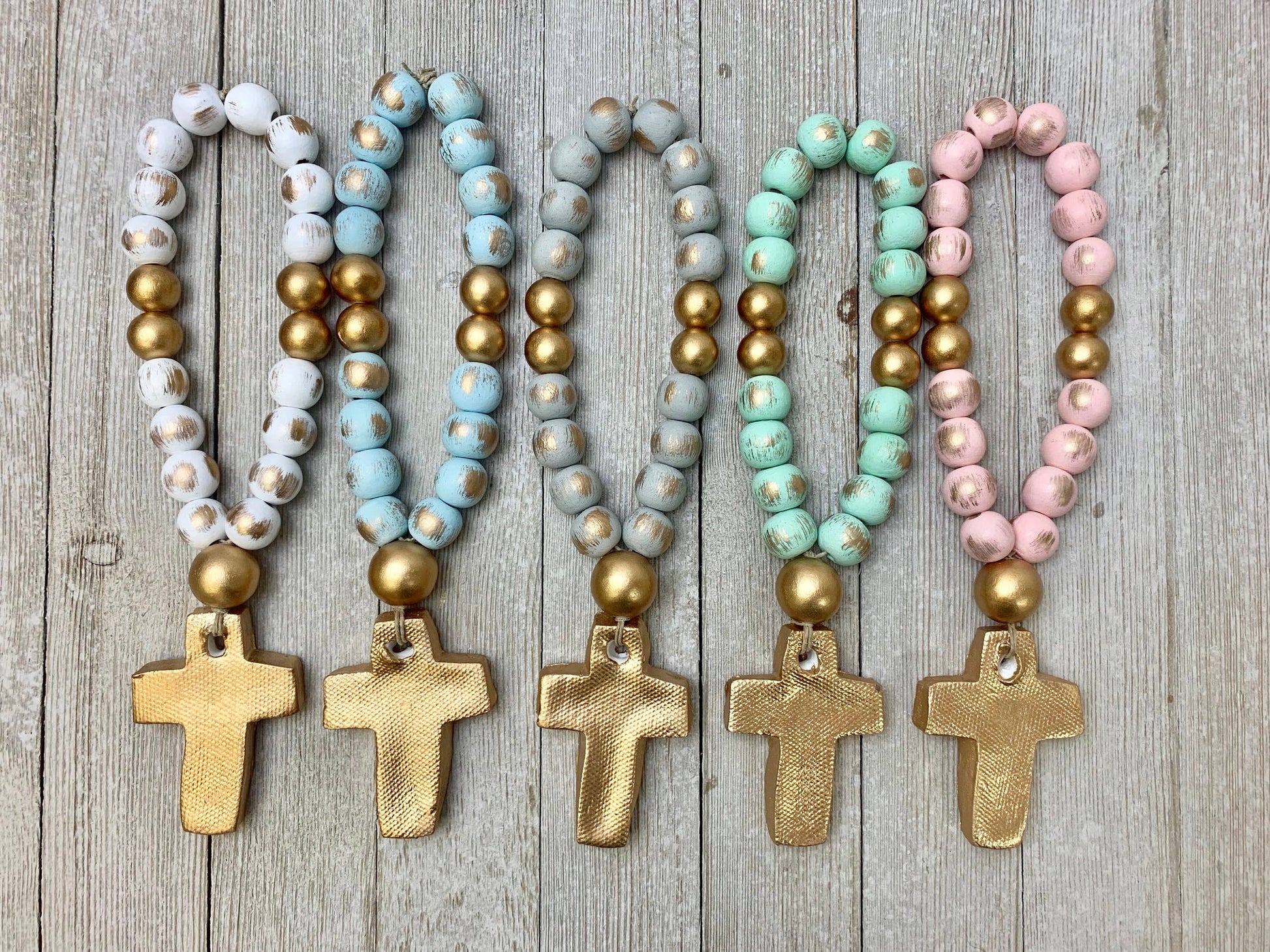 Set of five beaded baby blessing beads with cross pendants on a wooden surface. 