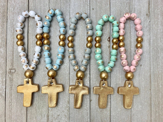 Set of five beaded baby blessing beads with cross pendants on a wooden surface. 