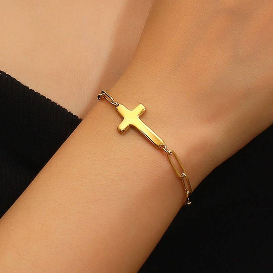 Gold cross bracelet on a wrist with a black background