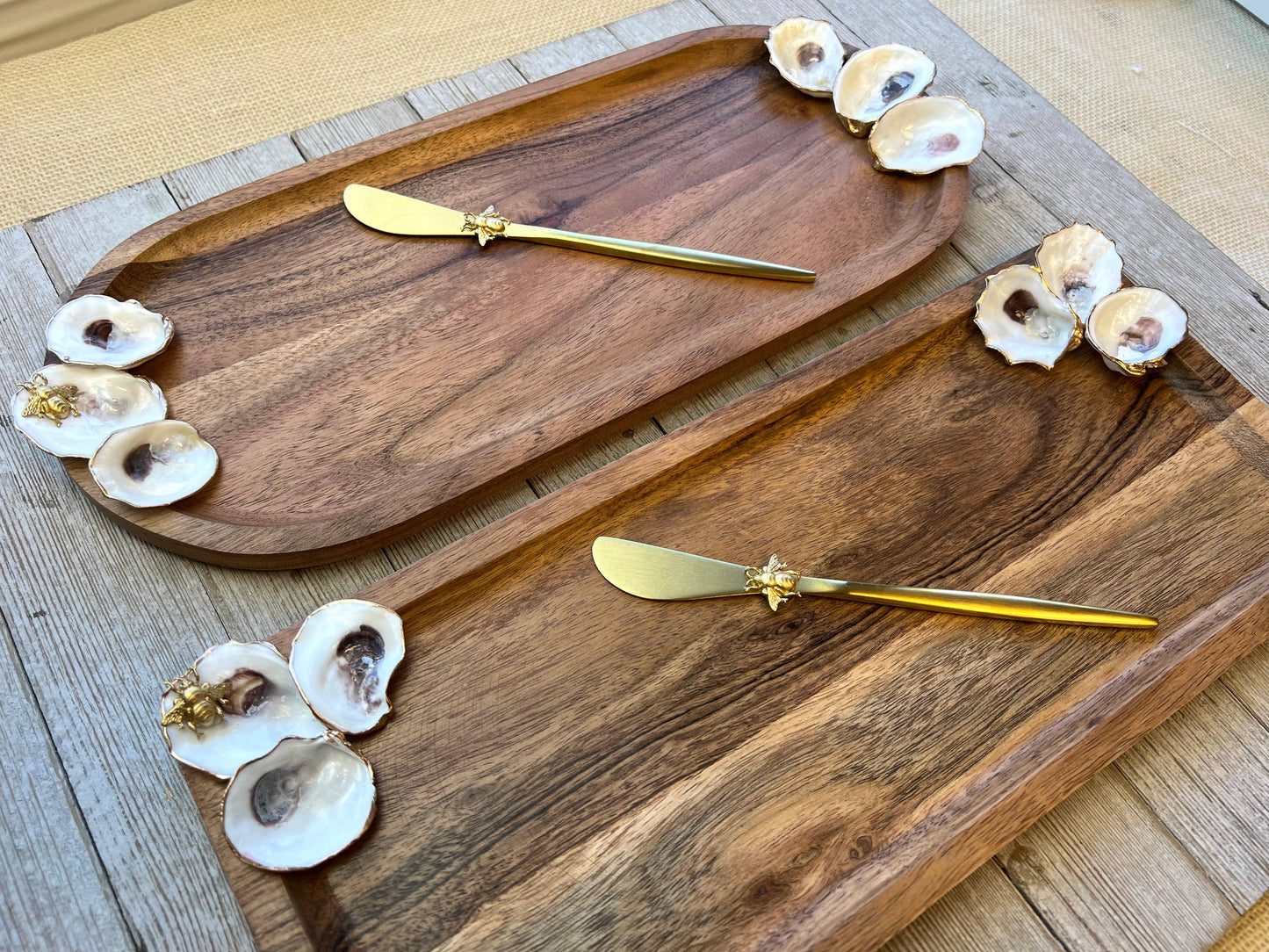 Wooden serving trays with gold spreaders and oyster shells on a wooden surface