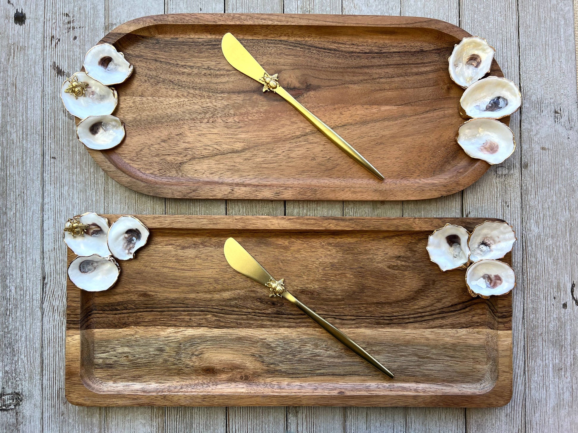 Two wooden trays with gold butter knives and oyster shells on a wooden surface.