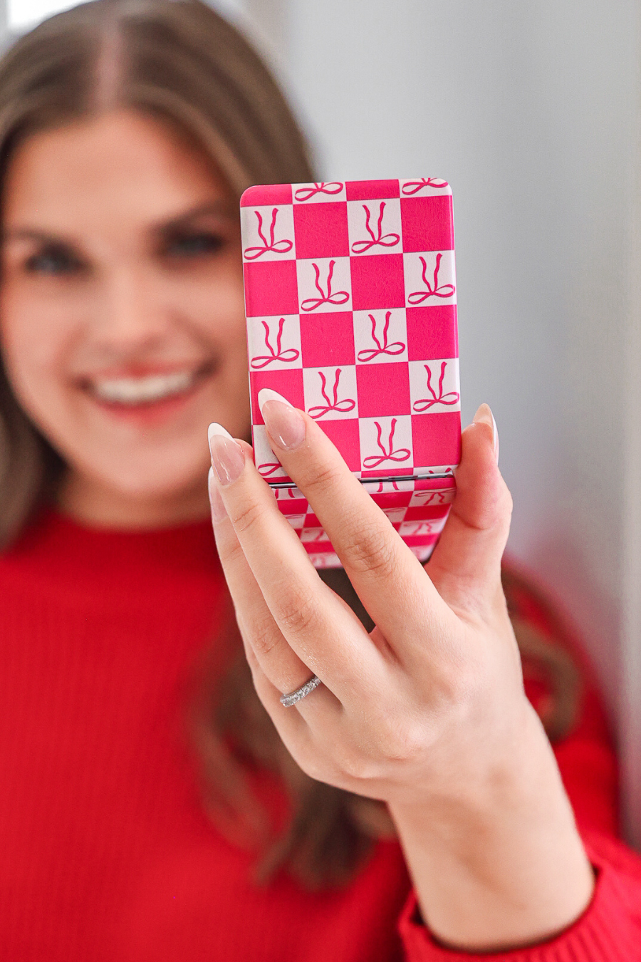 Person holding a pink and white checkered mirror with a bow pattern.